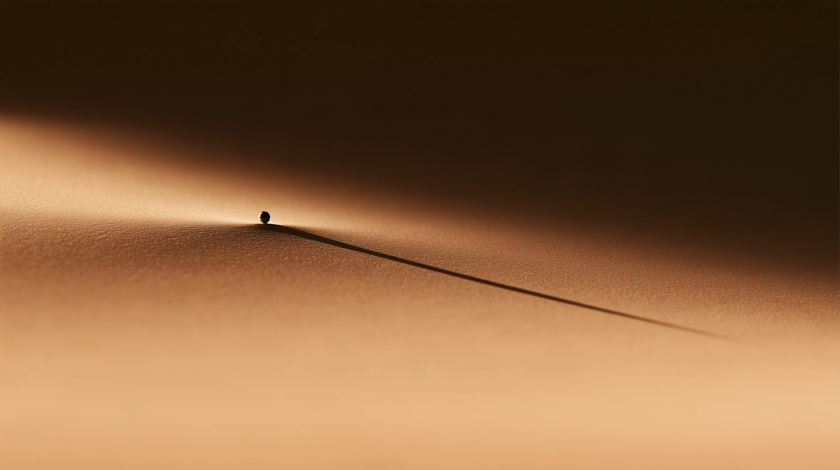 A small sphere resting at the edge of a ridge, casting one long shadow.